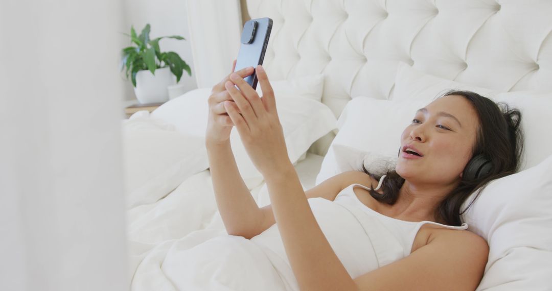 Woman Relaxing in Bed Using Smartphone and Wearing Headphones - Free Images, Stock Photos and Pictures on Pikwizard.com