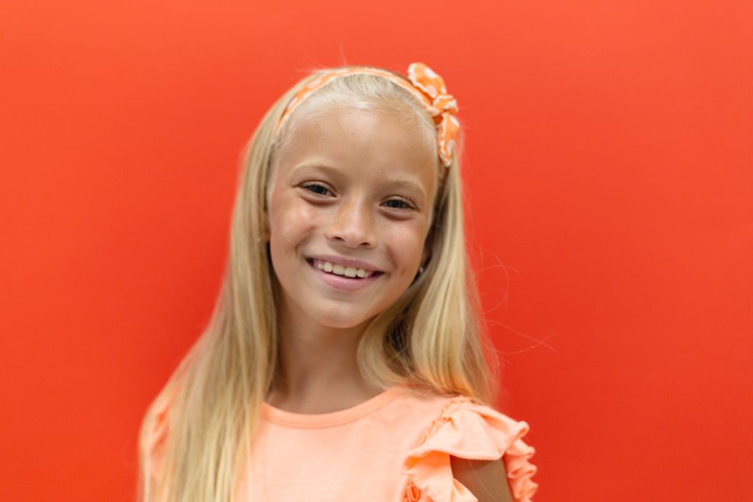 Smiling Blonde Elementary Schoolgirl Against Orange Background - Free Images, Stock Photos and Pictures on Pikwizard.com