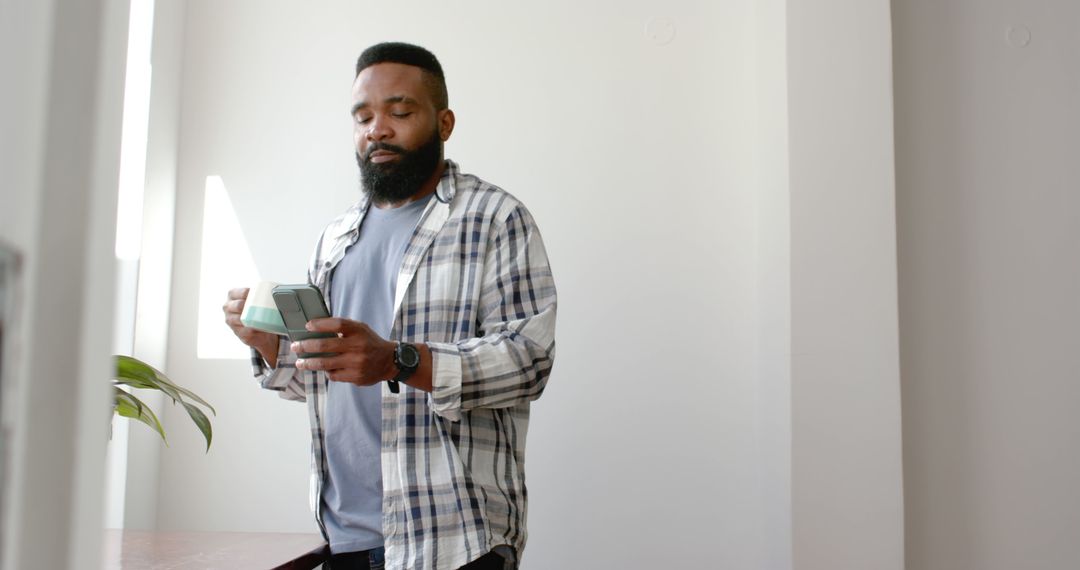 African American Man Holding Smartphone in Bright Room - Free Images, Stock Photos and Pictures on Pikwizard.com