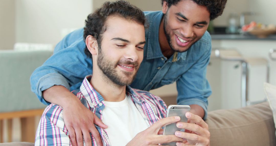 Two Young Men Smiling While Sharing Smartphone Moment at Home