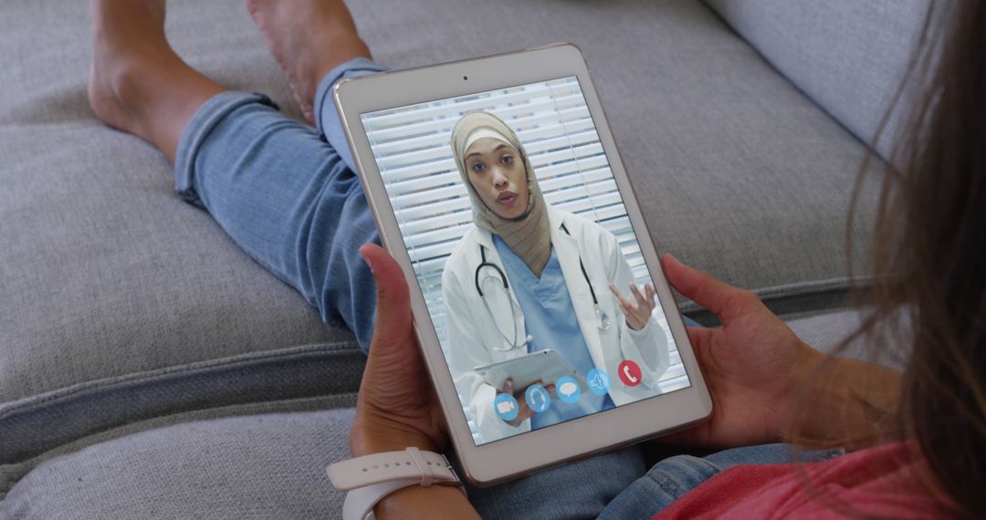 Woman on Sofa Using Tablet for Telemedicine with Female Muslim Doctor - Free Images, Stock Photos and Pictures on Pikwizard.com