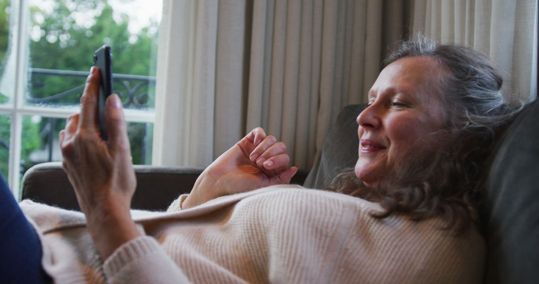 Smiling Middle-Aged Woman Relaxing on Couch Using Smartphone - Free Images, Stock Photos and Pictures on Pikwizard.com