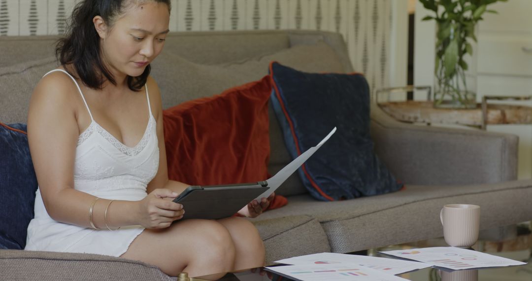 Woman Reviewing Documents with Tablet on Sofa in Modern Living Space