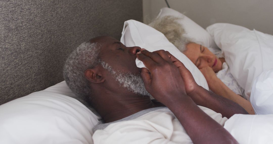 Senior Man Sick in Bed With a Cold Next to Sleeping Partner