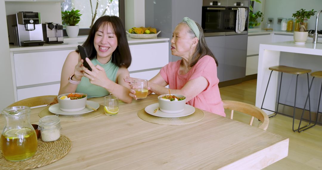 Granddaughter Sharing Smartphone with Smiling Grandma in Kitchen