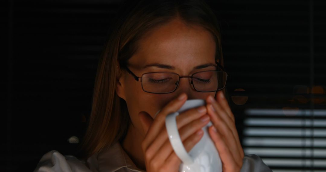 Woman Wearing Glasses Enjoying Hot Drink in Dimly Lit Room - Free Images, Stock Photos and Pictures on Pikwizard.com