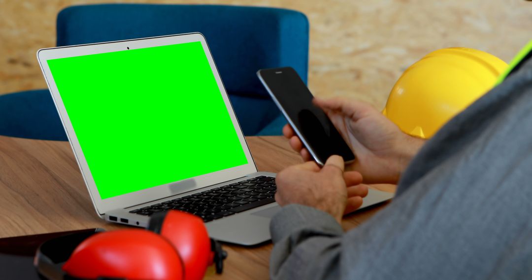 Construction worker holding smartphone next to laptop with green screen - Free Images, Stock Photos and Pictures on Pikwizard.com