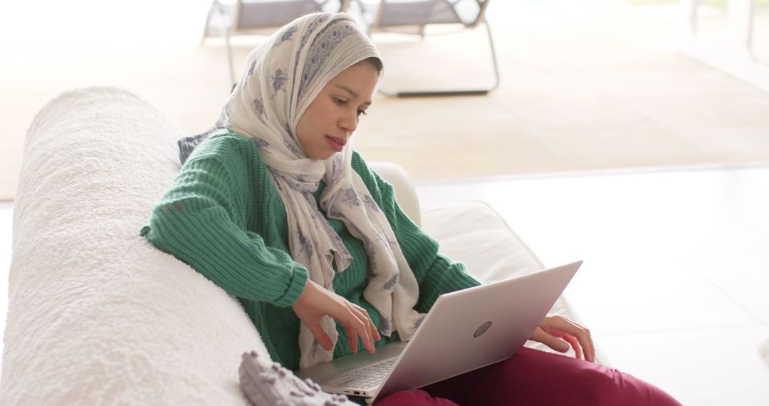 Woman in Hijab Using Laptop on Couch in Bright Living Room - Free Images, Stock Photos and Pictures on Pikwizard.com