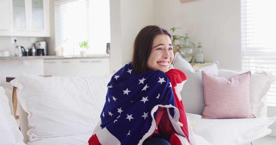 Excited Woman Watching Event Wrapped in USA Flag Inside Bright Living Room - Free Images, Stock Photos and Pictures on Pikwizard.com