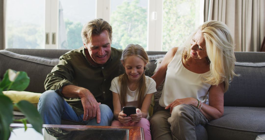 Grandparents Sitting with Granddaughter Looking at Smartphone in Living Room - Free Images, Stock Photos and Pictures on Pikwizard.com