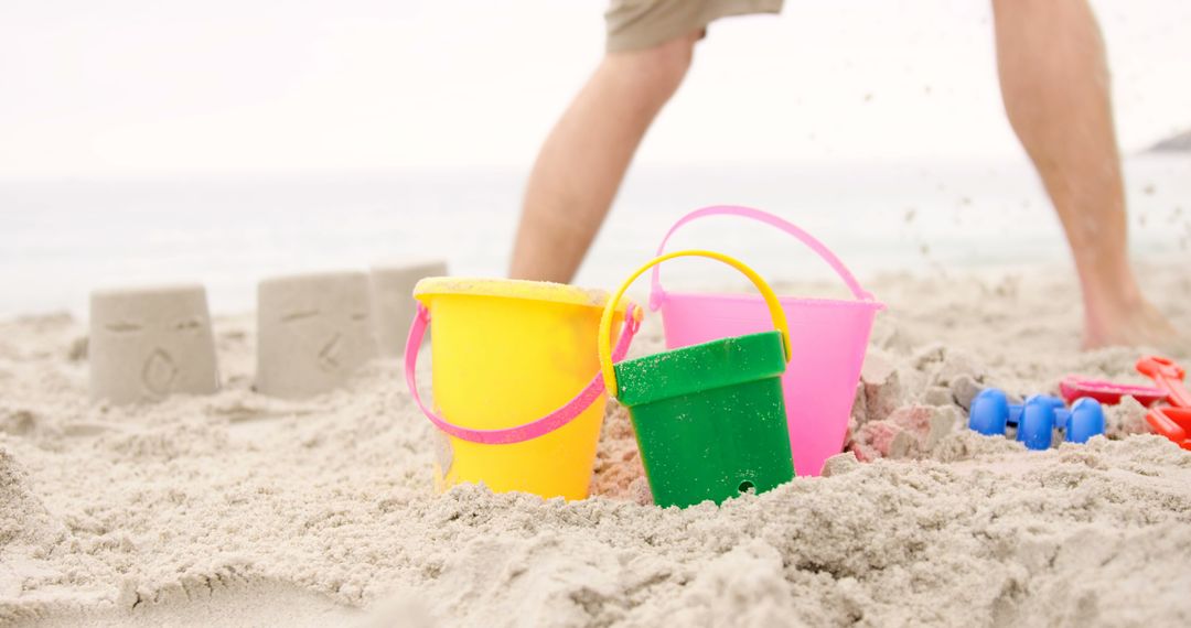 Colorful Sand Buckets on Beach with Person in Background - Free Images, Stock Photos and Pictures on Pikwizard.com