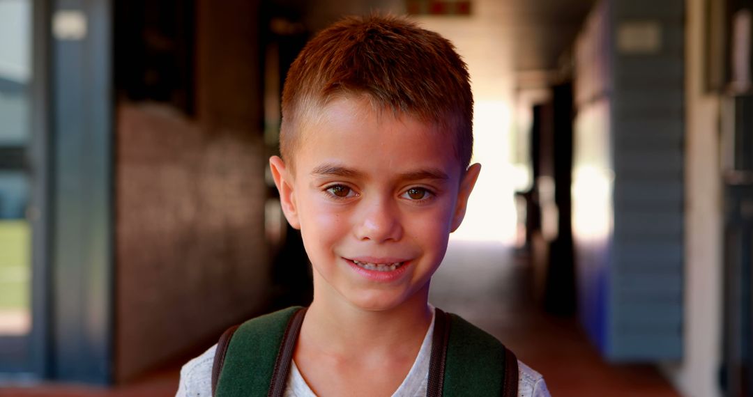 Smiling Young Boy in School Hallway Wearing Backpack