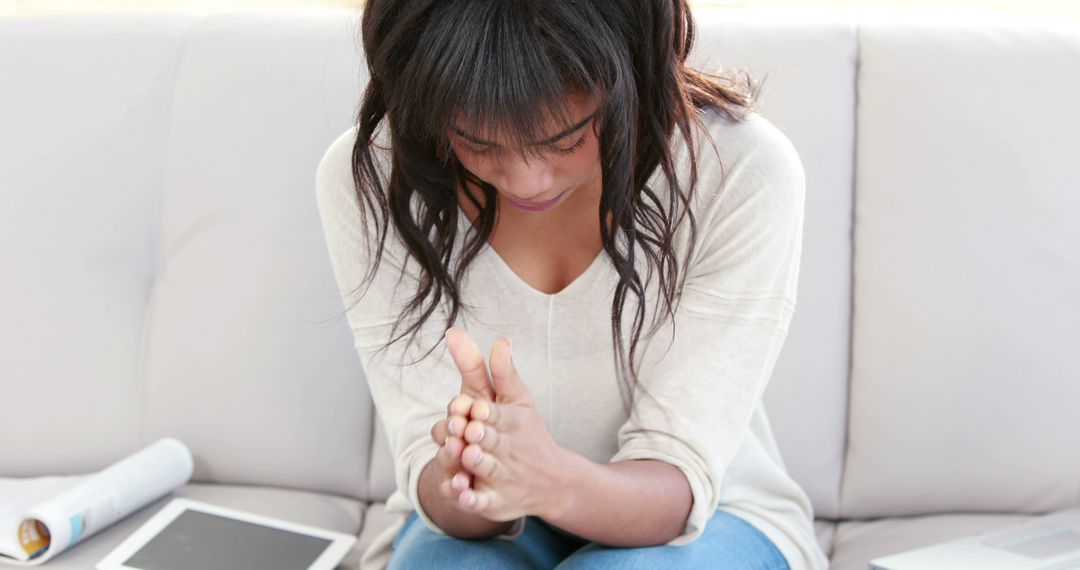 Stressed Young Woman Sitting on Couch Holding Hands Together - Free Images, Stock Photos and Pictures on Pikwizard.com