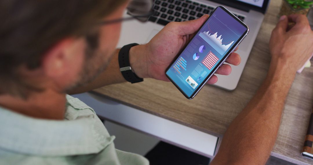 Man Analyzing Data on Smartphone with Laptop Background