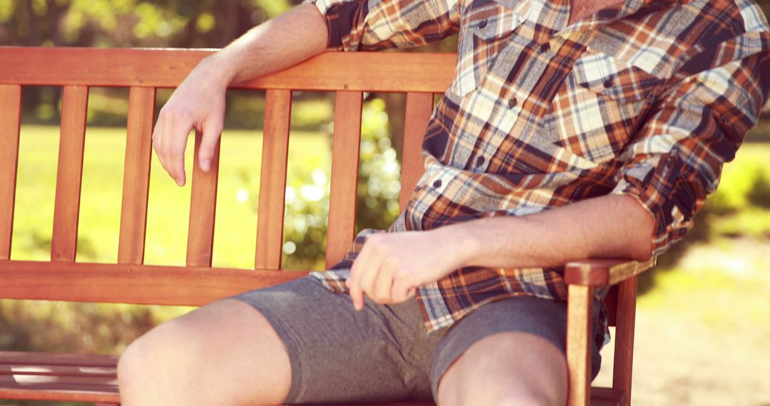 Relaxed Young Man Sitting on Park Bench in Plaid Shirt and Casual Shorts - Free Images, Stock Photos and Pictures on Pikwizard.com