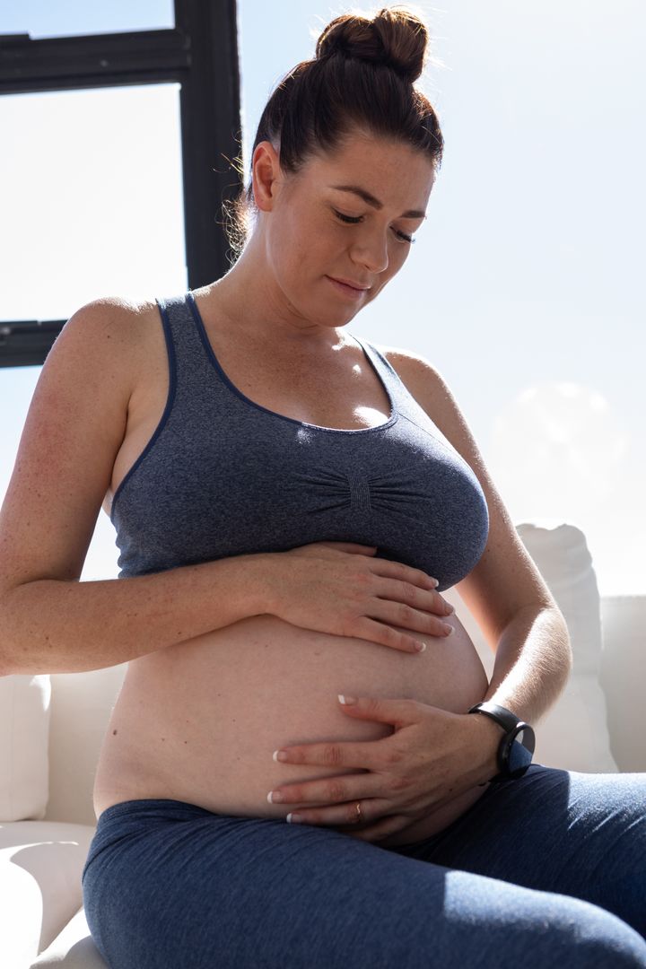 Pregnant Woman in Sportswear Relaxing on Sofa by Window