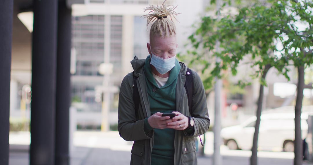 Young Man with Dreadlocks Wearing Medical Mask Checking Phone Outdoors - Free Images, Stock Photos and Pictures on Pikwizard.com