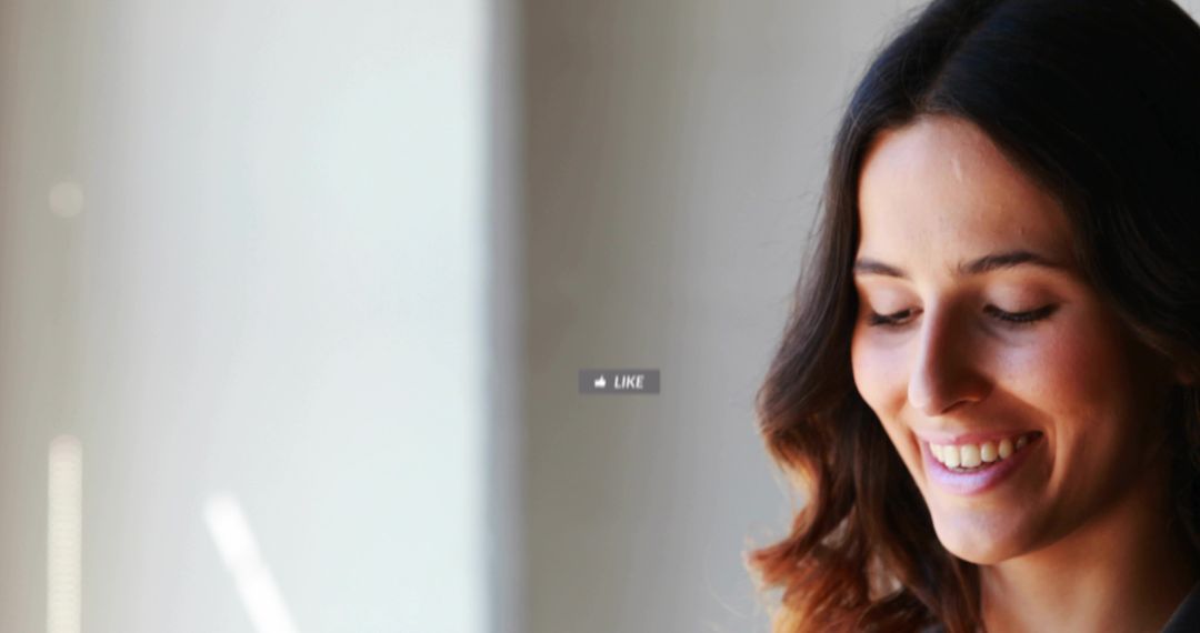 Smiling white woman looking down by window with like icon overlay and soft natural light