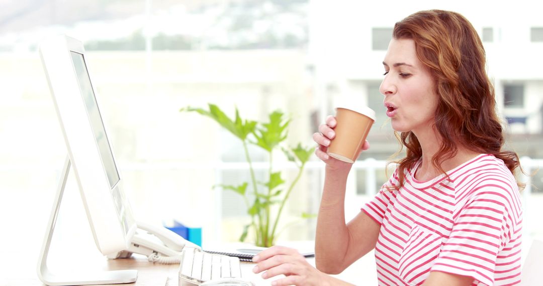 Woman Working at Computer and Drinking Coffee in Well-Lit Office - Free Images, Stock Photos and Pictures on Pikwizard.com