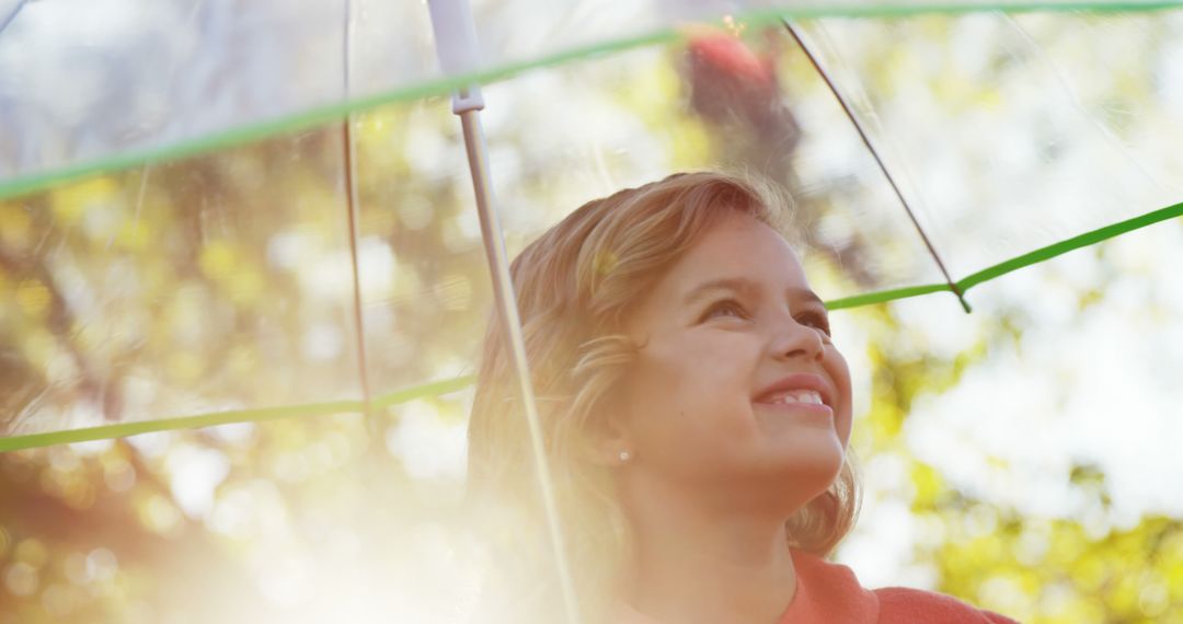 Smiling Girl Under Clear Umbrella in Sunlit Park - Free Images, Stock Photos and Pictures on Pikwizard.com