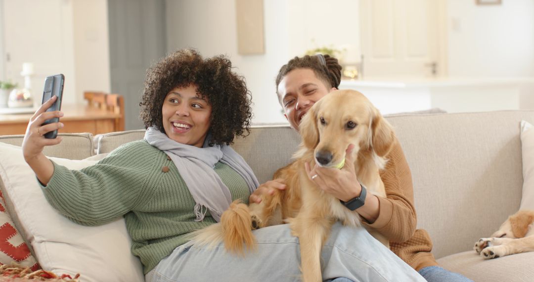 Diverse couple snapping selfie with golden retriever on cozy sunlit sofa