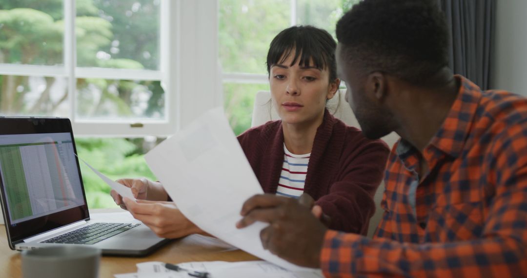 Diverse Couple Collaborating at Home with Laptop and Documents