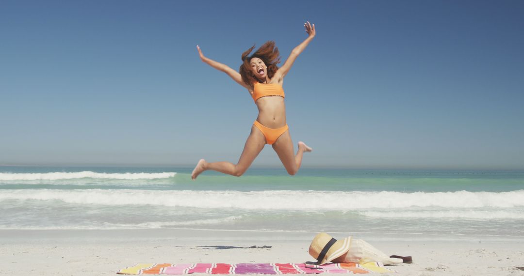 Woman Jumping in Joy on a Sunny Beach with Towel and Hat - Free Images, Stock Photos and Pictures on Pikwizard.com