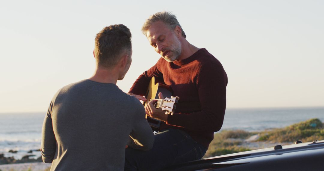 Man playing guitar by the beach with friend listening - Free Images, Stock Photos and Pictures on Pikwizard.com