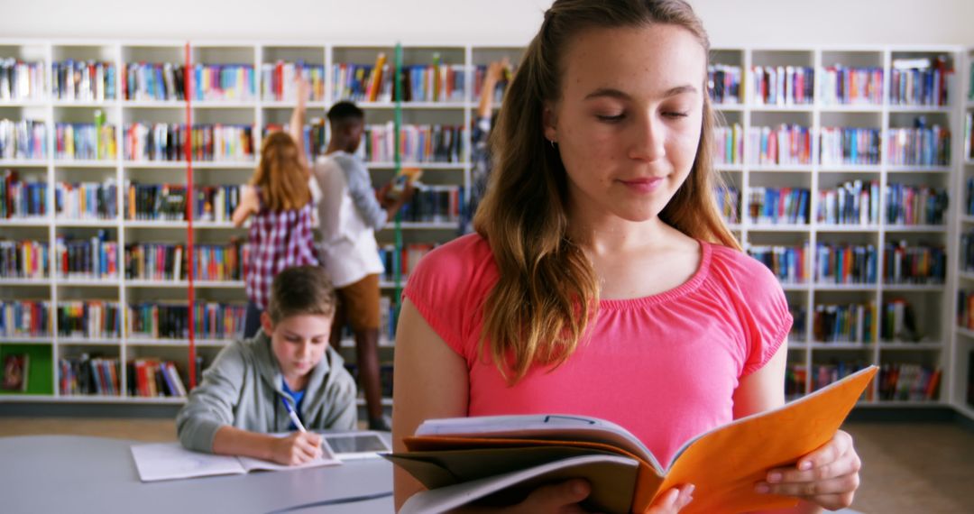 Teen Girl Reading Book in School Library with Classmates Studying in Background - Free Images, Stock Photos and Pictures on Pikwizard.com