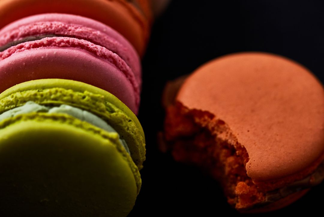 Close-up row of vibrant macarons on black background featuring bitten orange macaron