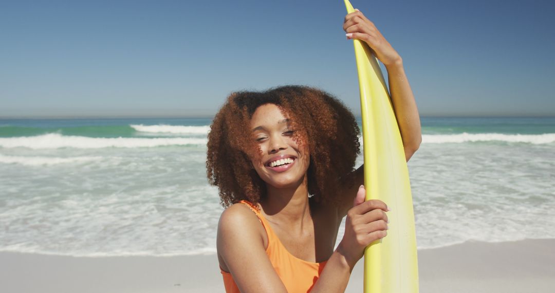 Biracial woman with curly hair standing on beach with surfboard and laughing - Free Images, Stock Photos and Pictures on Pikwizard.com