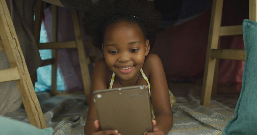 Young African American Girl Smiling While Using Tablet Inside Fort - Free Images, Stock Photos and Pictures on Pikwizard.com