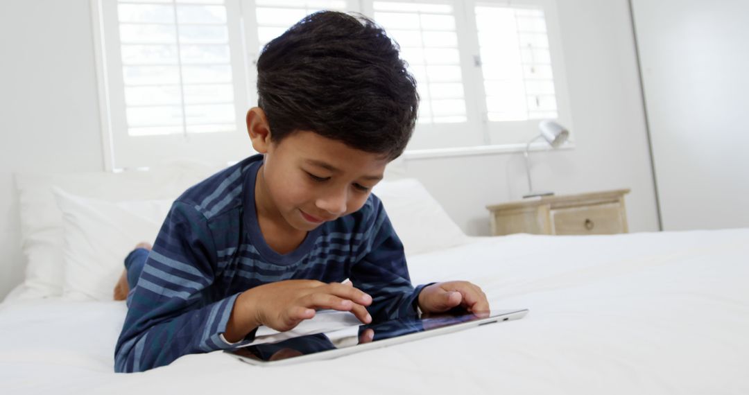 Young Boy Using Tablet Device While Lying on Bed at Home - Free Images, Stock Photos and Pictures on Pikwizard.com