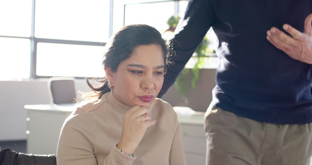 Thoughtful woman collaborating with coworker during focused team meeting in modern office