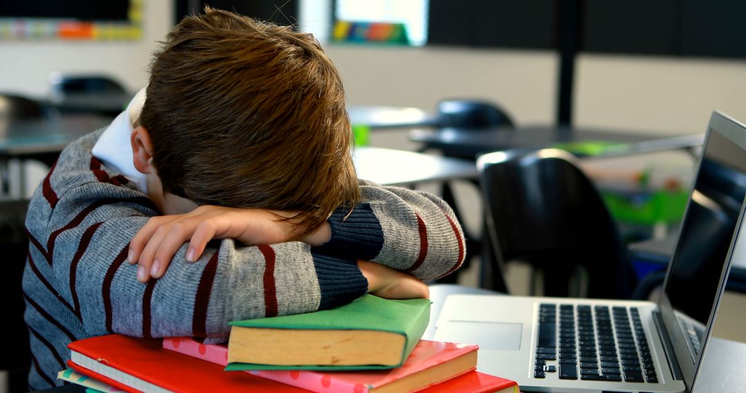 Tired Boy Leaning on Books and Laptop in Classroom