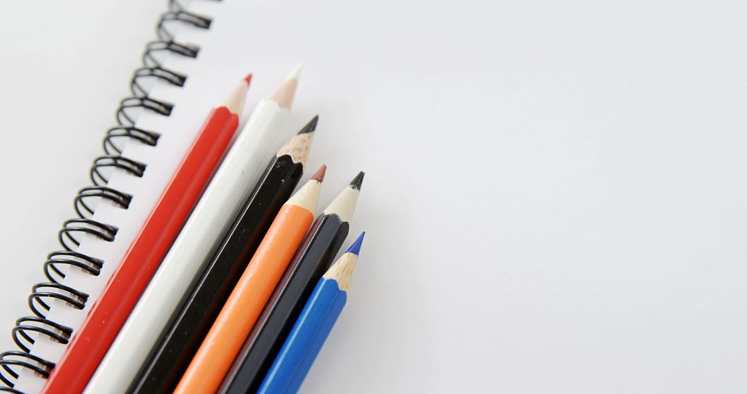 Colored pencils lie next to a spiral notebook on a white background, with copy space - Free Images, Stock Photos and Pictures on Pikwizard.com