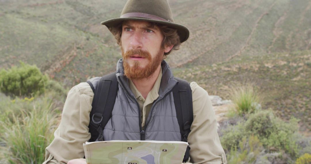 Red-Bearded Hiker Studying Map on Rugged Hillside for Navigation and Route Planning