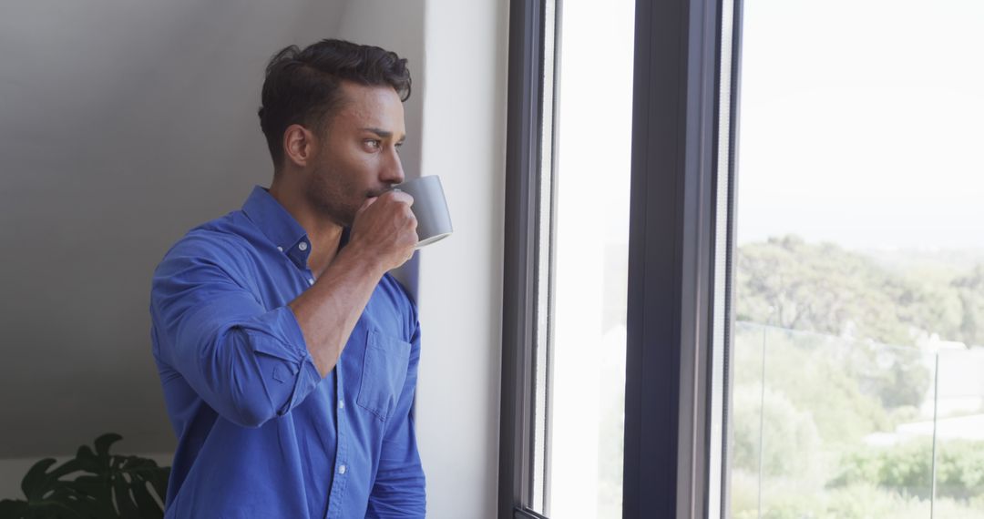 Man in Blue Shirt Drinking Coffee While Looking Out Window - Free Images, Stock Photos and Pictures on Pikwizard.com