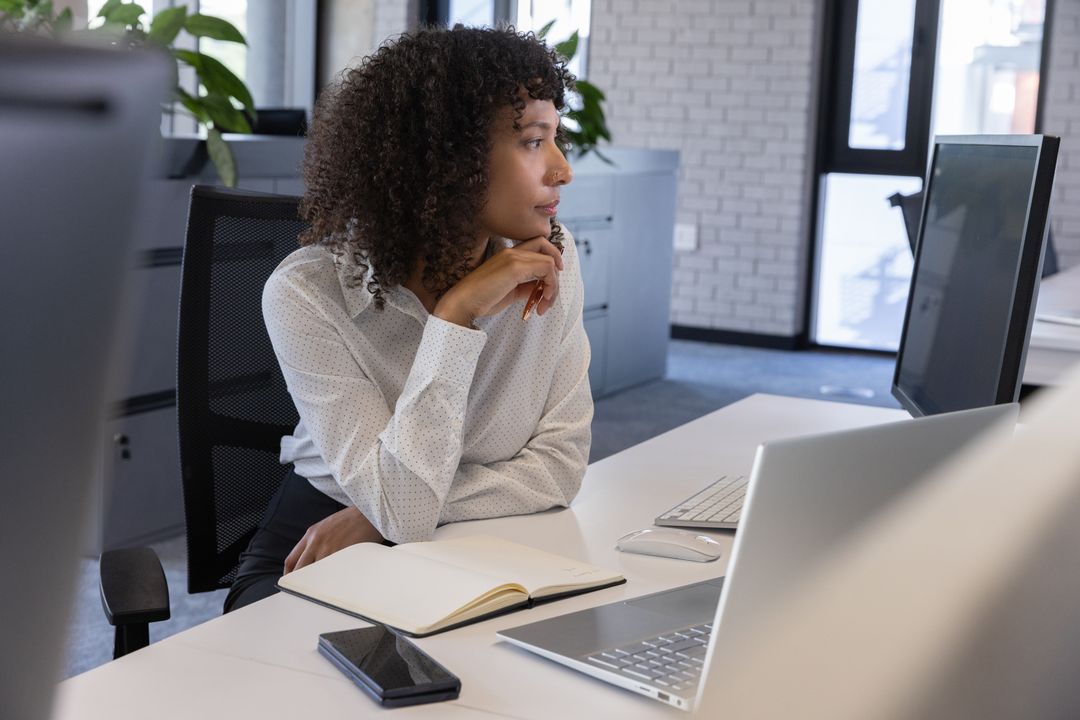 Focused Woman at Office Desk with Notebook and Laptop