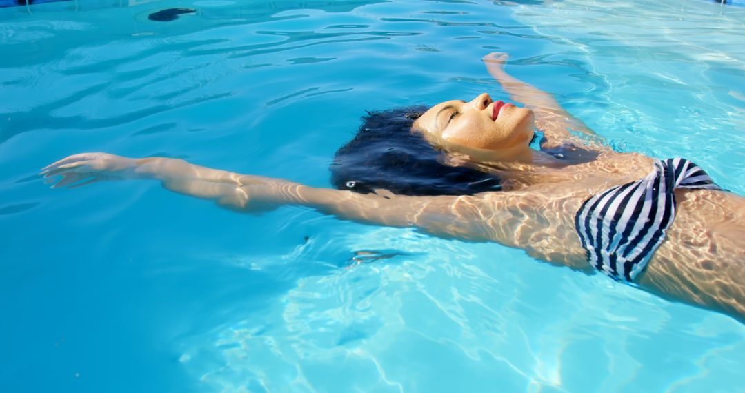 A young biracial woman is floating in pool, wearing a striped swimsuit - Free Images, Stock Photos and Pictures on Pikwizard.com