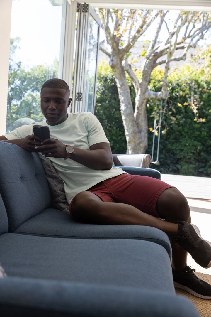 Man Relaxing on Sofa with Smartphone Near Sliding Doors