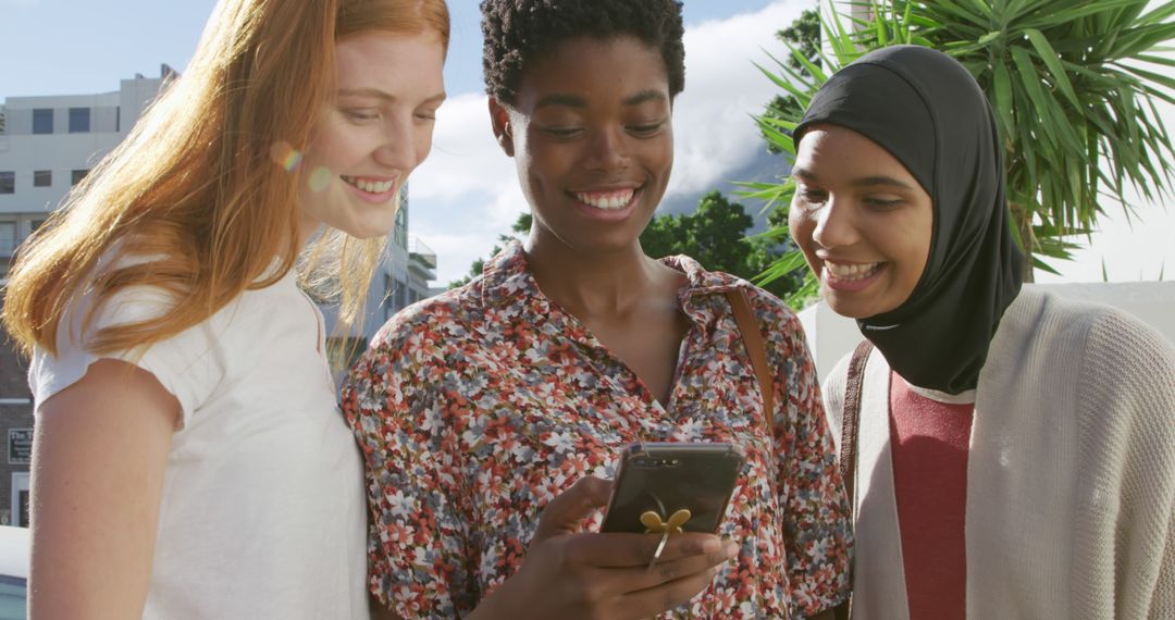 Diverse group of women smiling and looking at smartphone outdoors - Free Images, Stock Photos and Pictures on Pikwizard.com