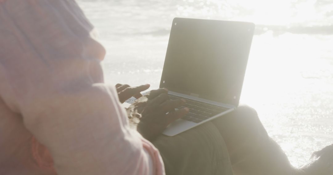 Person Typing on Laptop by Beach at Sunset with Sun Reflection - Free Images, Stock Photos and Pictures on Pikwizard.com