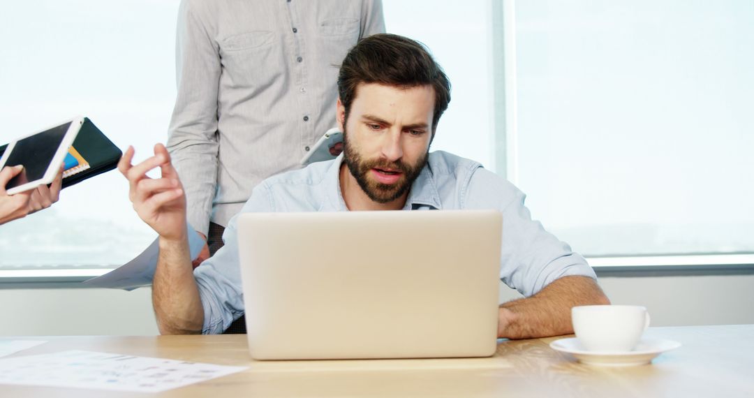 Stressed Businessman Working on Laptop with Colleagues in Office - Free Images, Stock Photos and Pictures on Pikwizard.com