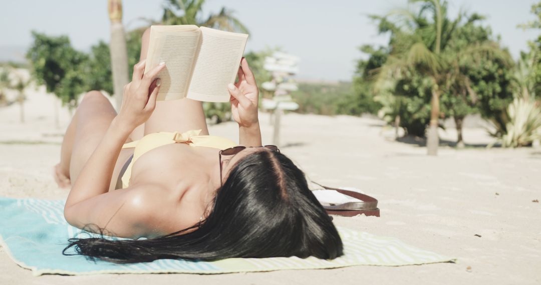 Hispanic woman in sunglasses lying on back on beach reading book, copy space, slow motion - Free Images, Stock Photos and Pictures on Pikwizard.com