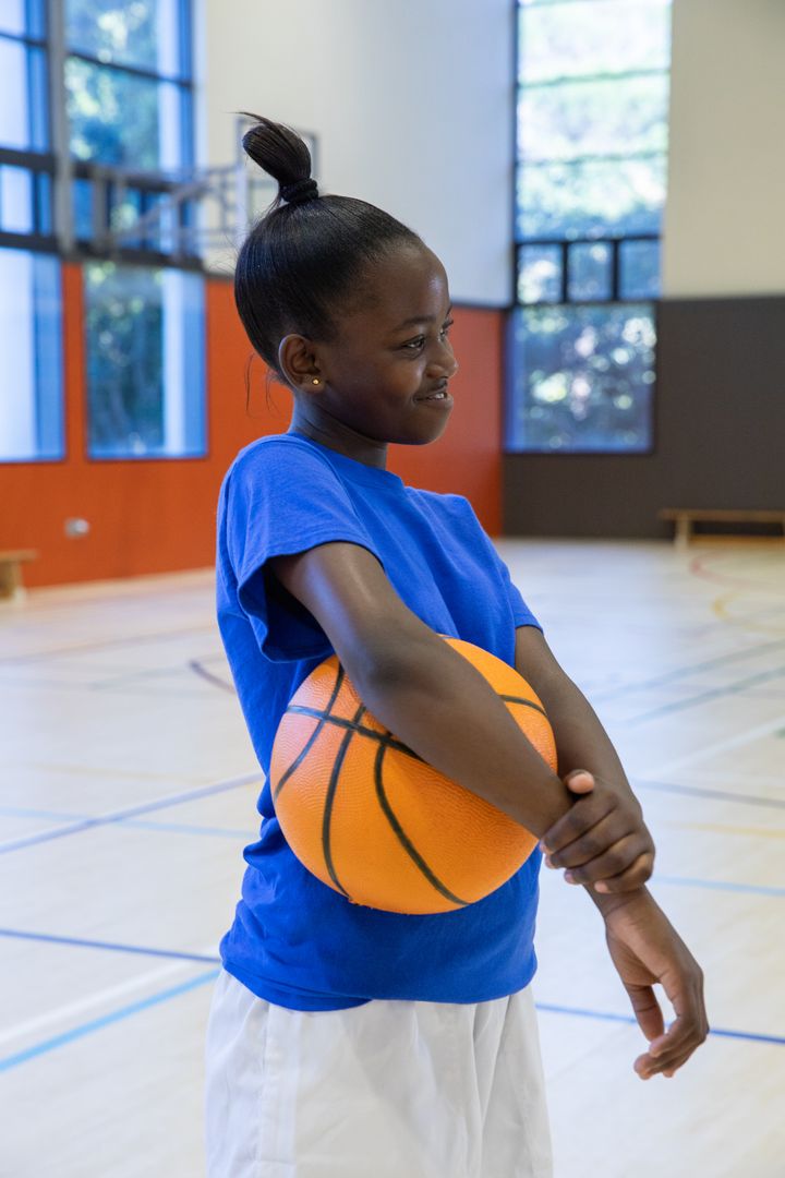 Youthful Enthusiasm: Girl Stretching with Basketball in Gymnasium