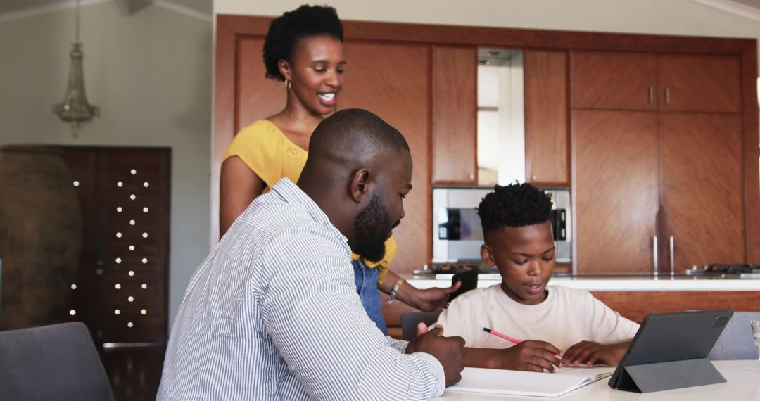African American parents helping son with homework using tablet at modern kitchen table