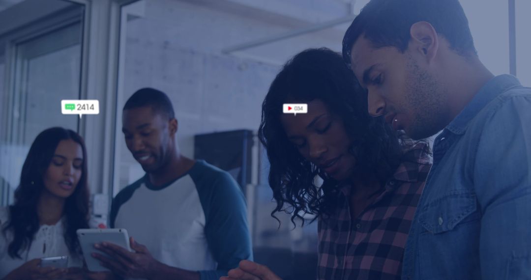 Collaborating team leaning over tablet in modern open-plan workspace with mobile devices