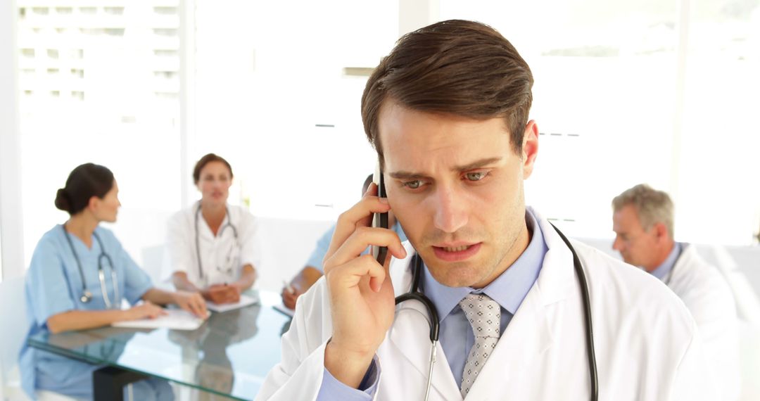 Stressed Doctor Talking on Phone in Hospital with Colleagues Meeting - Free Images, Stock Photos and Pictures on Pikwizard.com