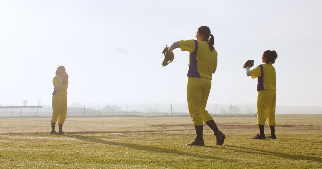 Diverse Female Team Practicing Softball at Dawn in Vibrant Yellow Uniforms